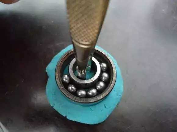 用鑷子或別的相近的物體越過內圈，同時向滾珠的方向用力頂住